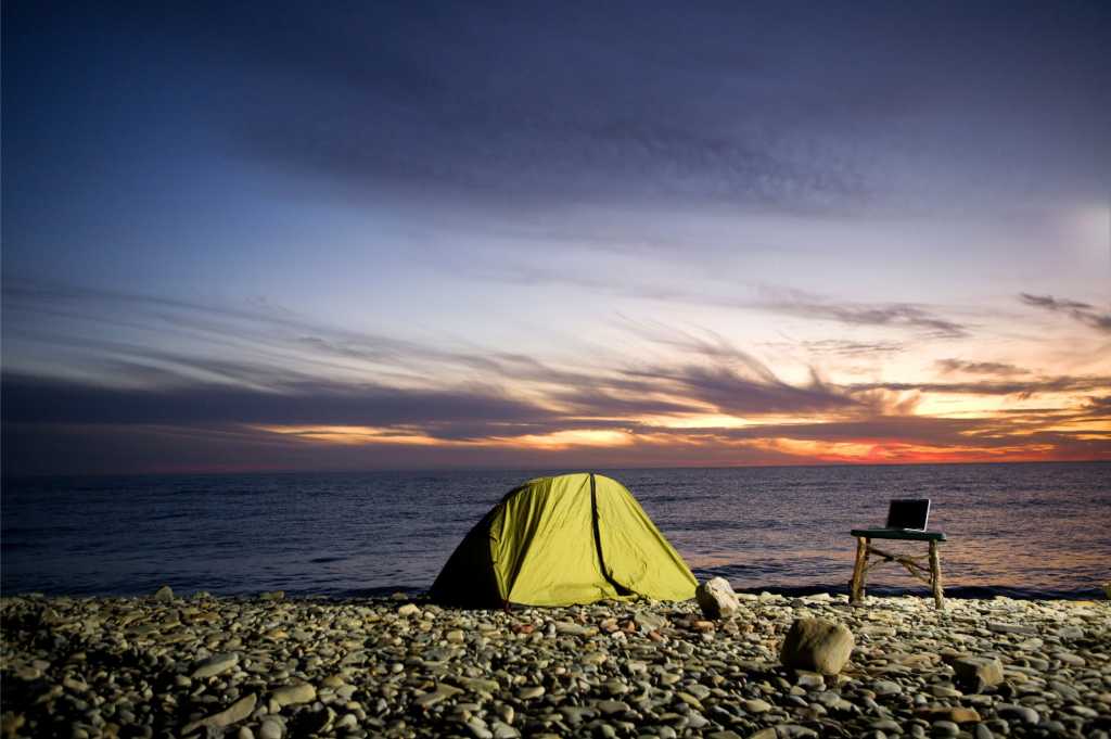 Digital nomad's beach tent and laptop camp at sunset.